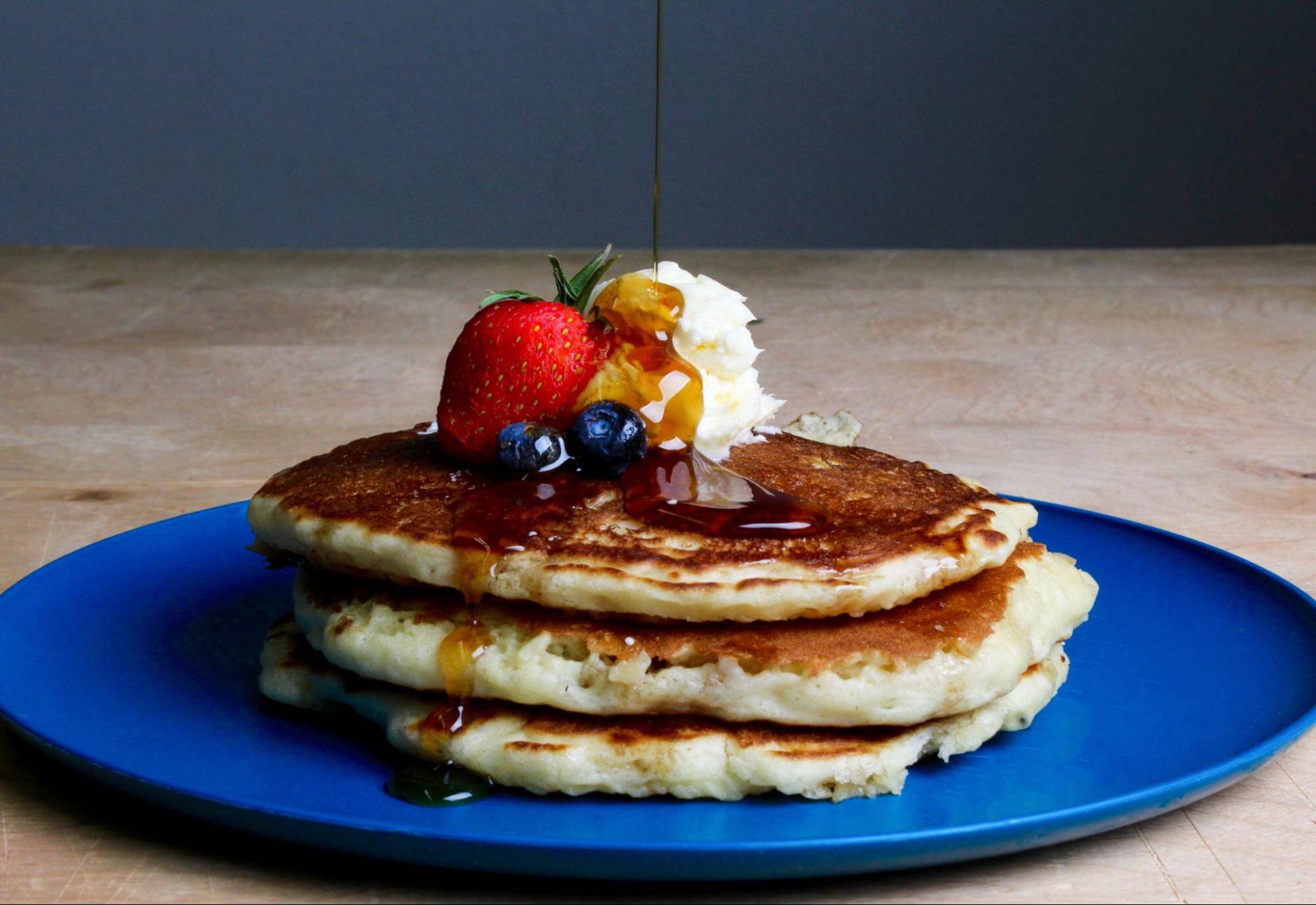 A stack of pancakes topped with fresh fruit, whipped cream and maple syrup.